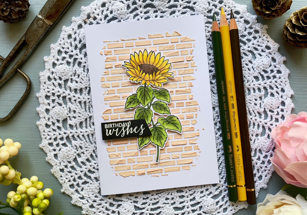 Make a handmade Birthday card by colouring a sunflower using the Faber Castell Plychromos colouring pencils and creating a brick background using a stencil and embossing paste with Distress inks.