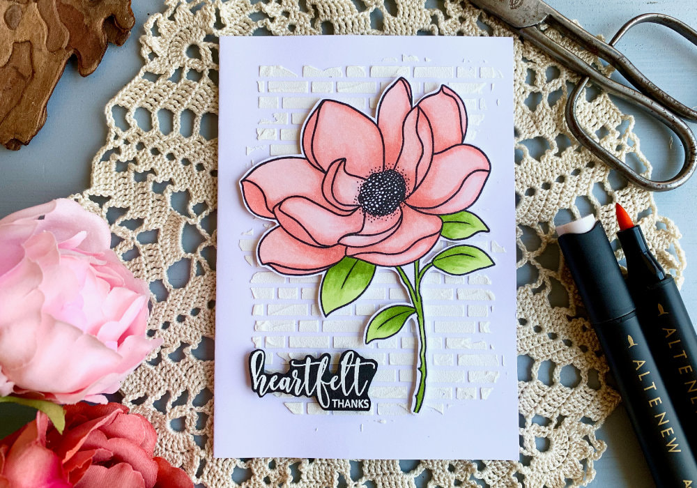 Handmade Thank You greeting card with a big stamped Magnolia flower coloured in light red shades using alcohol markers. The flower is adhered onto a white card base with a brick background created with a stencil and embossing paste .