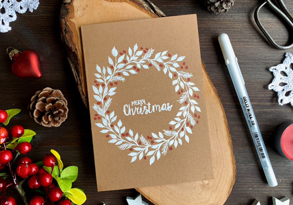 Simple DIY Christmas card with a hand-drawn wreath using a white gel pen for the leaves, red pen for berries and card base made out of a craft card stock.