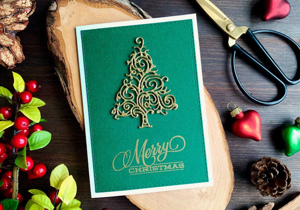 Handmade Christmas card with a glittery Christmas tree, die-cut and heat embossed with a golden embossing powder and Merry Christmas greeting, placed on a green card stock and white card base.