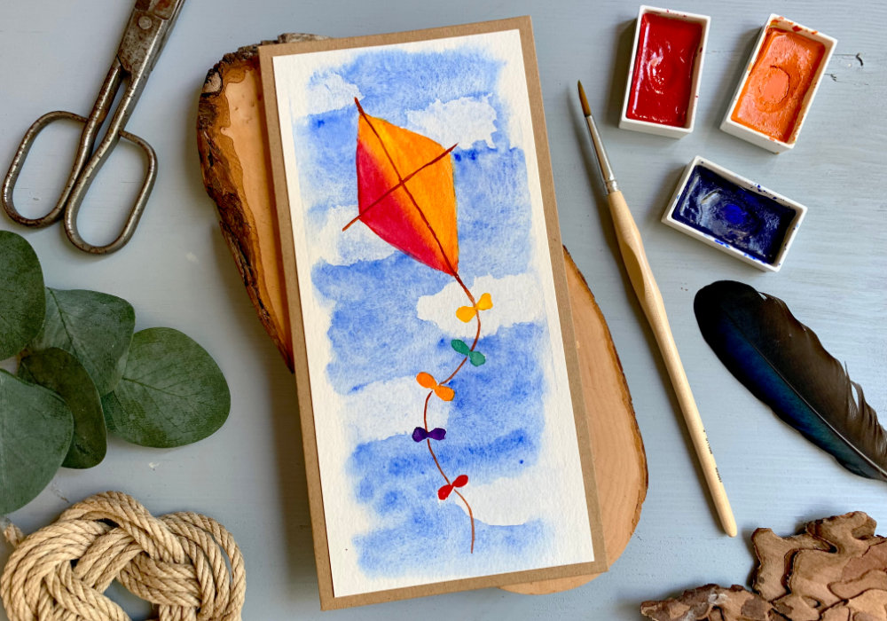 Handmade greeting card with a hand-drawn kite, painted with watercolours flying in the sky. 