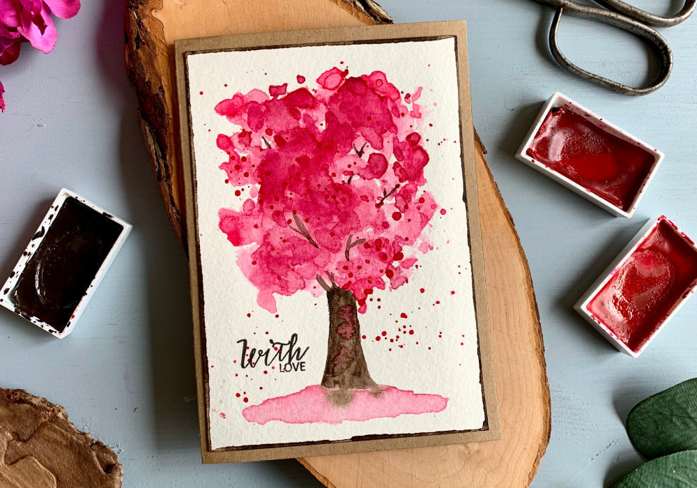 DIY greeting card with a hand-painted cherry tree using pink watercolours and the ink smooshing technique. The greeting says With Love, stamped with a black ink.
