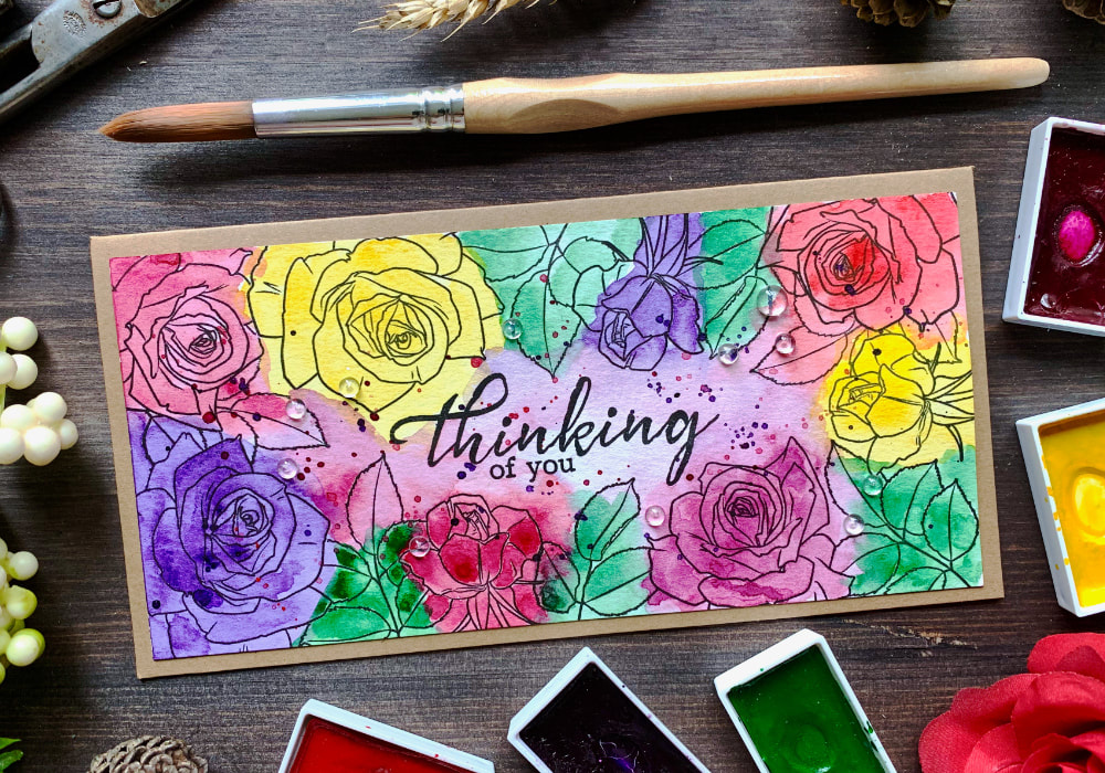 Handmade card with stamped roses along the edges creating frame and coloured with watercolours in multiple colours - pinks, purples, reds, yellows and greens - doing the messy watercolour technique.
