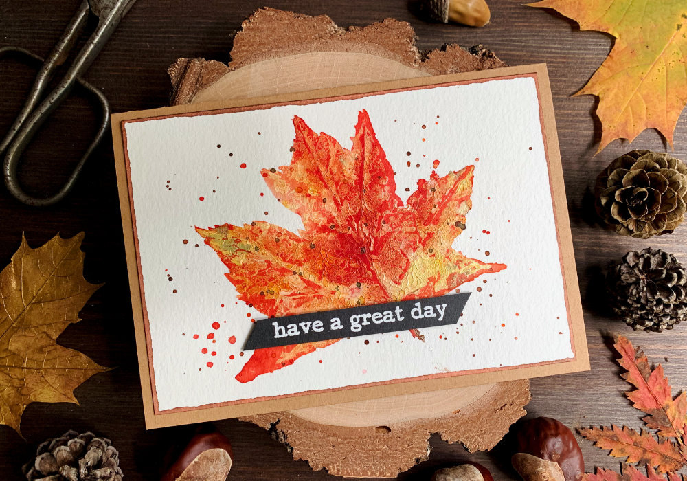 Handmade Birthday card with a stamped maple leaf using white acrylic paint and coloured white the Brusho watercolour powders using reds and oranges. The greeting 