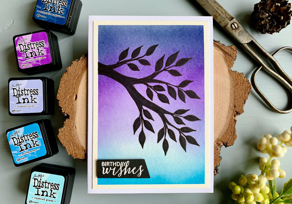 Handmade Birthday card with a sunset sky created with Distress inks - Chipped Sapphire, Wilted Violet, Shaded Lilac, Tumbled Glass and Salty Ocean and a silhouette of a tree branch and leaves drawn with a black marker.
