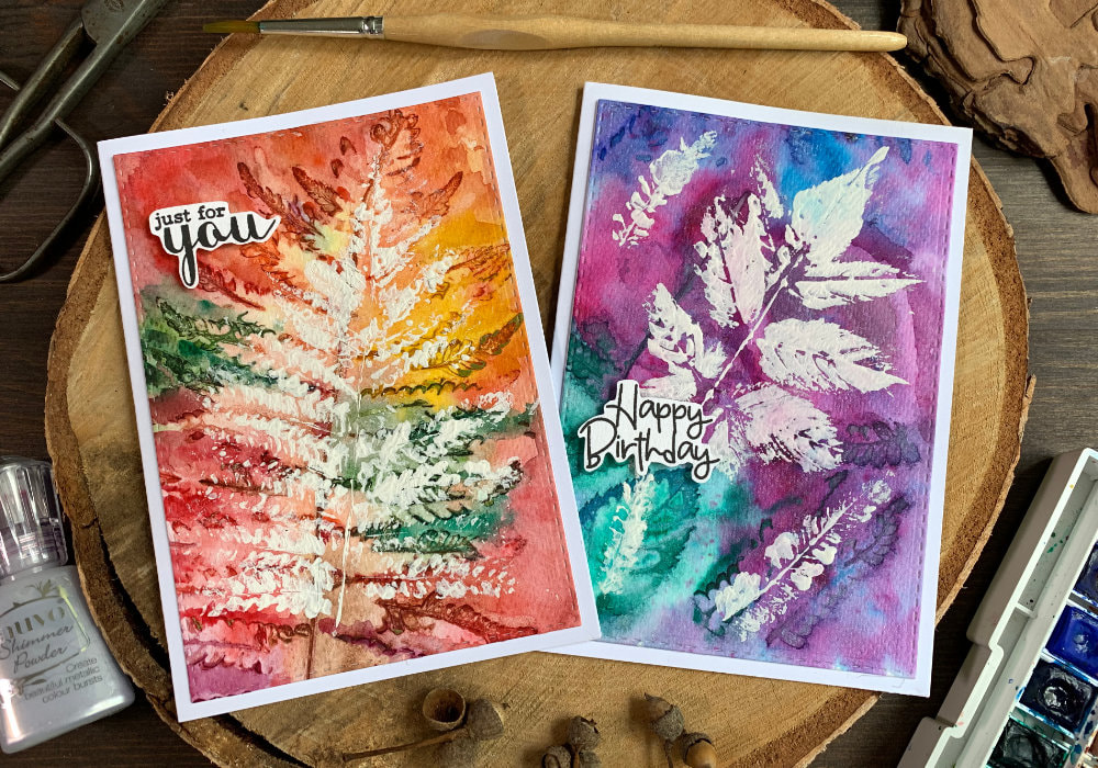 Handmade autumnal greeting card with leaf pattern created by using real leaves and watercolours to create impressions and a white gouache to stamp a leaf over the pattern. One card has a typical autumnal background the other is purple, pink and blue.