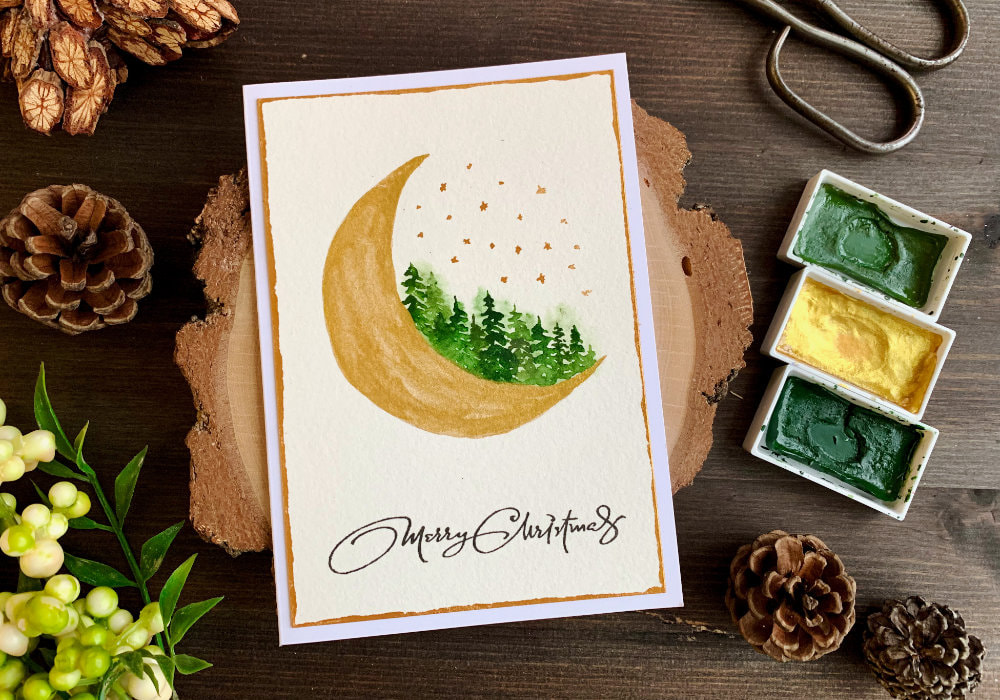 Modern, nontraditional Christmas card with a hand-drawn quarter moon painted with golden watercolours and green loose watercolour forest.