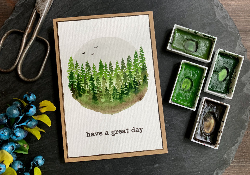 Handmade greeting card with  green watercolour fir trees, painted into a circle shape. The sky is painted grey with three black birds. The greeting below the painting says Have A Great Day.