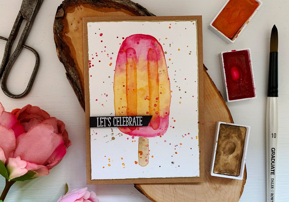 Handmade Birthday card with a watercolour ice lolly / popsicle, pink on the top and bottom and orange in the middle. The greeting says Let's Celebrate and it's stamped on a black card stock, heat embossed in white and cut it out into a banner.