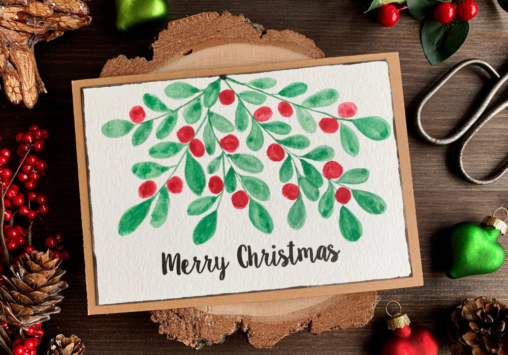Simple Christmas card with a hand painted watercolour mistletoe with red berries and greeting that is stamped in black and says Merry Christmas.