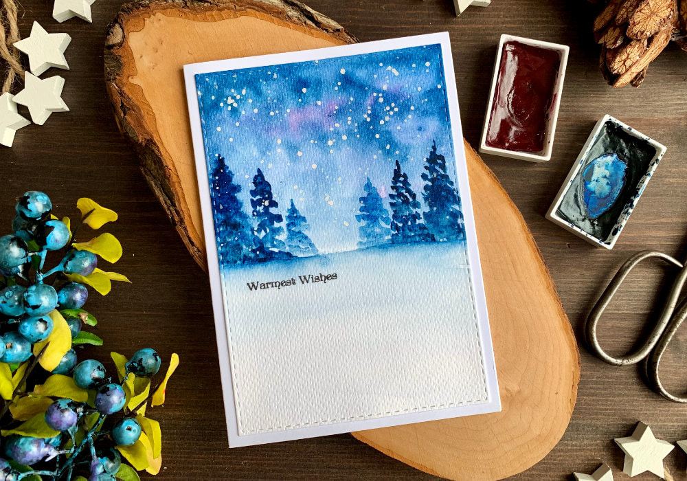 Handmade Christmas card with a watercolour winter forest scene at night. The forest is painted in the top half of the card and the bottom is left white. The greeting says Warmest Wishes and is stamped below the trees.