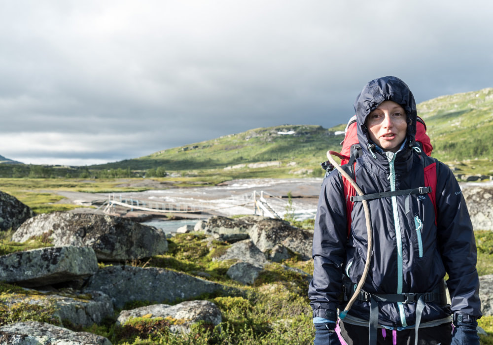 Photo of me wearing my red backpack, wrapped in a rain jacket looking very cold, while hiking in Hardangervidda in Norway.