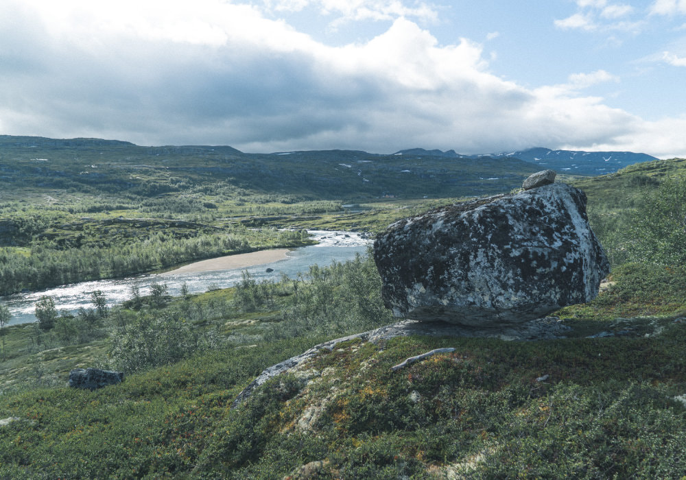 Landscape of Hardangervidda, with a river in the valley and mountains in the background.