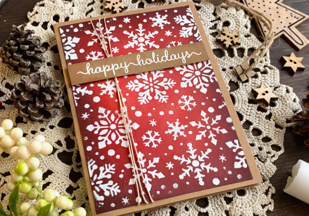 Handmade Christmas card with a red Distress ink background using the inks Ground Espresso, Aged Mahogany, Barn Door and Candied Apple, covered with snowflakes stamped with a stencil and heat embossed in white.