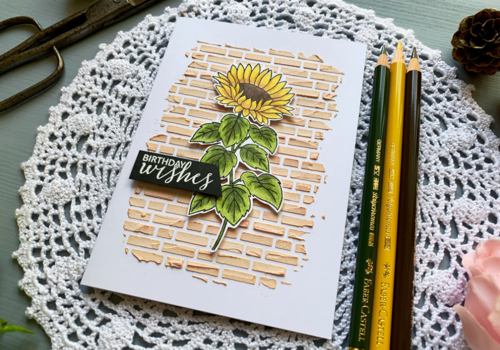 Simple Happy Birthday card with a sunflower coloured with colouring pencils from Faber Castell and textured brick background using a stencil and embossing paste.