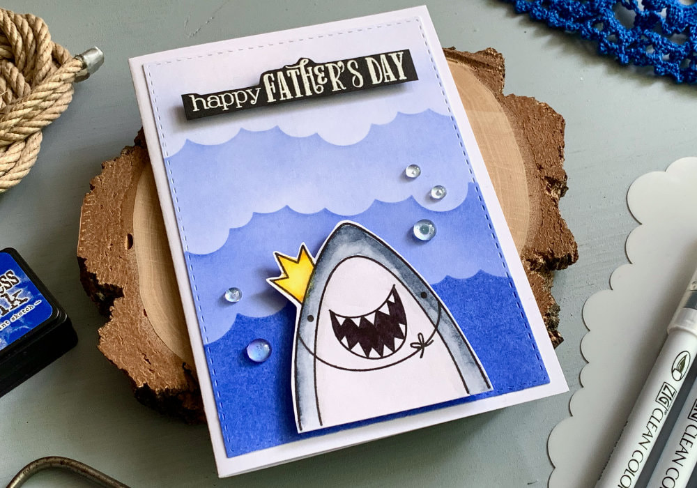 Simple handmade card for Father's day with a background with waves created using a stencil and blue ink and a stamped smiling shark with a crown. 