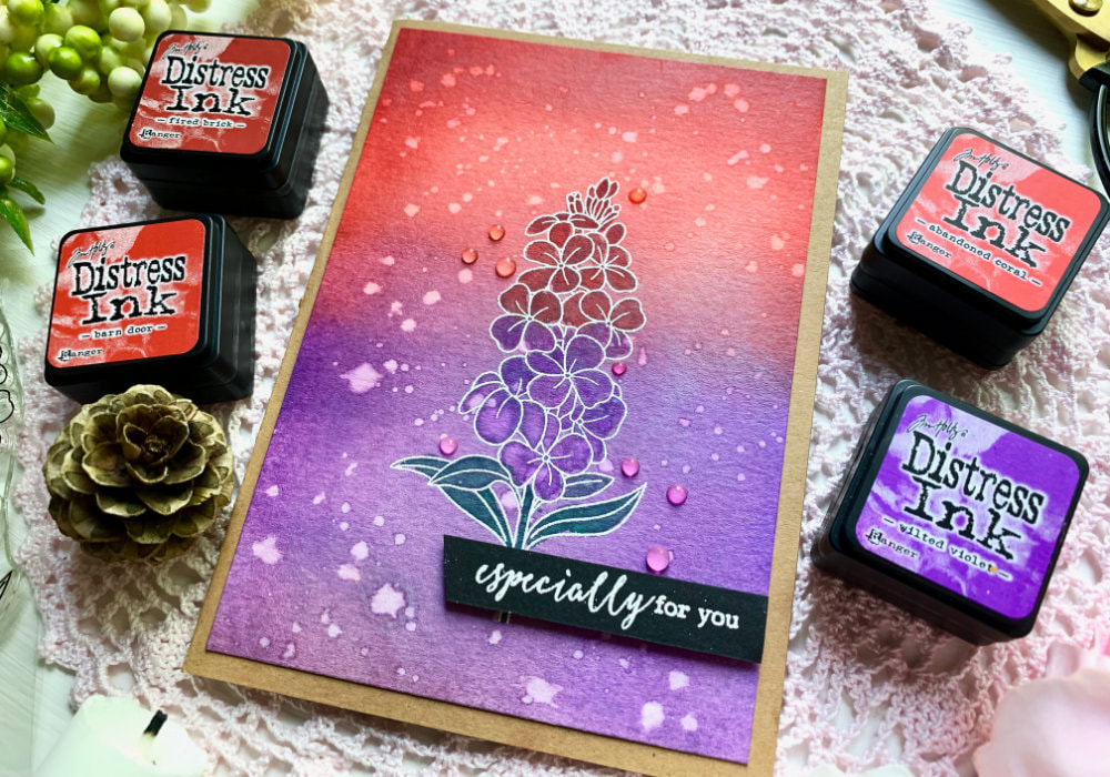 Handmade greeting card with a red and pruple background created with Distress inks. Flower is stamped and heat embossed in white and painted with the same Distress inks as well as green one, to enhance the colour.