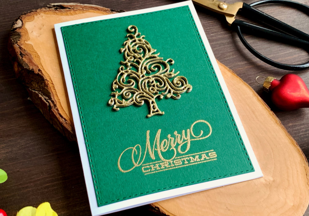 Handmade Christmas card with a glittery Christmas tree, die-cut and heat embossed with a golden embossing powder and Merry Christmas greeting, placed on a green card stock and white card base.