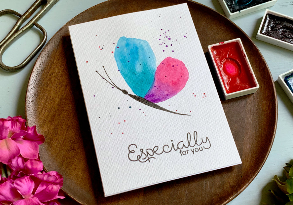 Handmade card for Birthday with a hand painted simple watercolour butterfly from a side with top wing in the blue-green and lower wing pink-purple. And black body. Painted on a white watercolour card stock, with a black greeting saying Especially For You.
