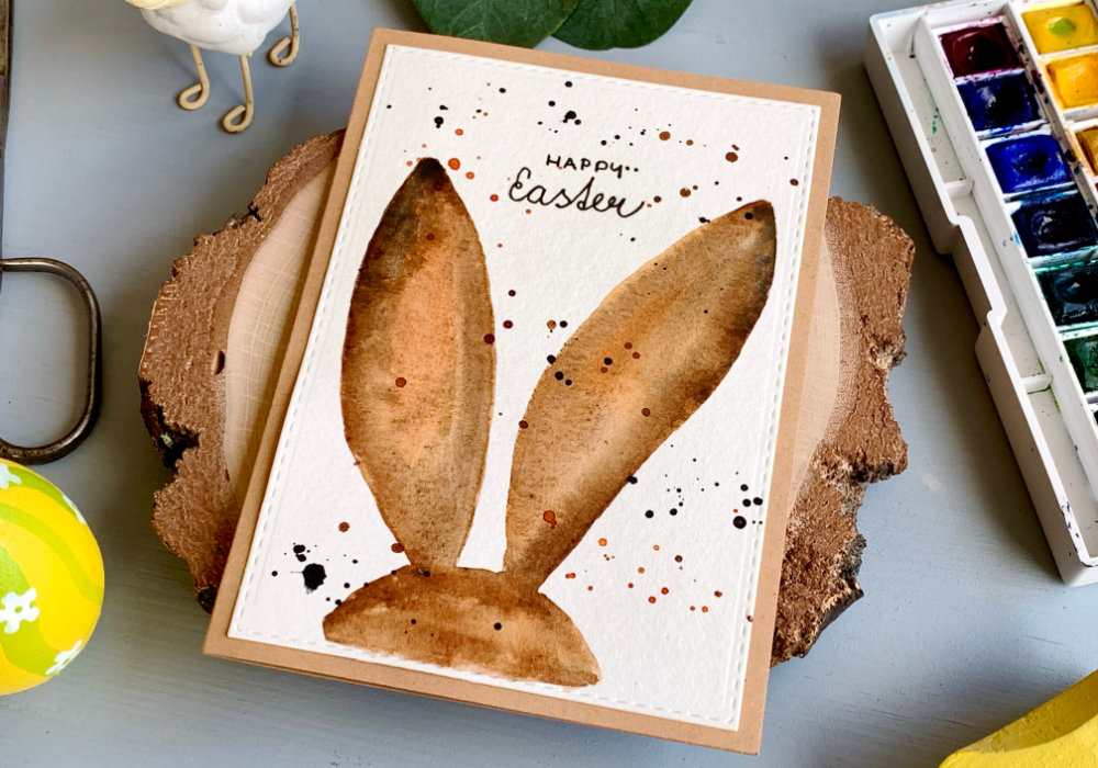 Handmade Easter card with hand drawn bunny ears from the back, painted with watercolours using different shades of brown. The greeting is handwritten and says Happy Easter.