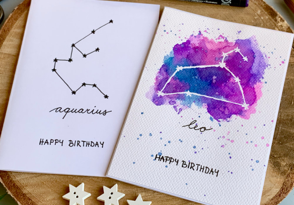 Two handmade Birthday cards. One with hand black drawn Zodiac star sign Aquarius and the other with a white Leo sign and blue and pink watercolour background. 