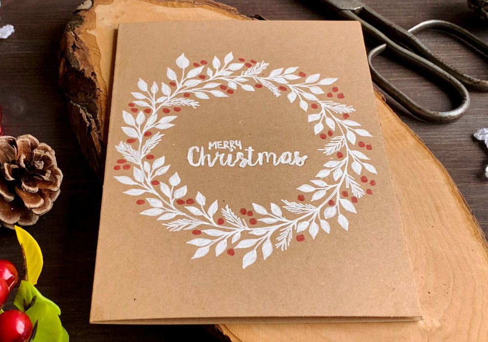 Simple DIY Christmas card with a hand-drawn wreath using a white gel pen for the leaves, red pen for berries and card base made out of a craft card stock.