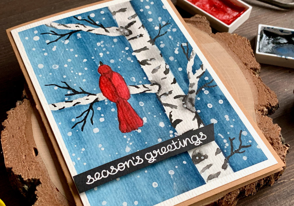 Handmade Christmas card with watercolour snowy winter scene with a birch tree and a red bird sitting on a brunch. The greeting saying 
