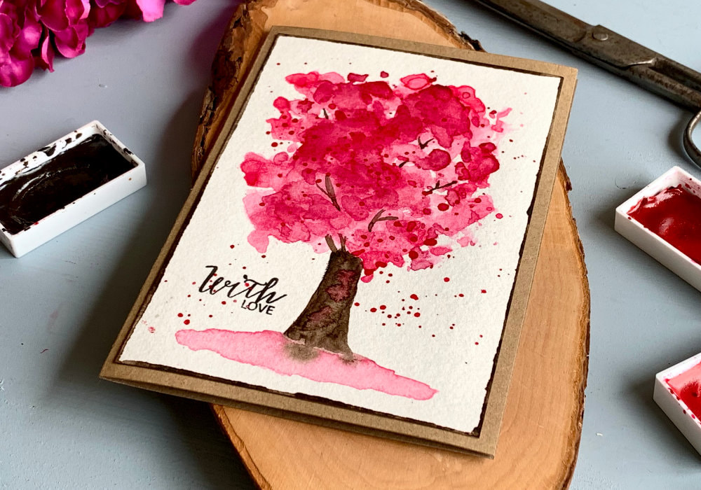 DIY greeting card with a hand-painted cherry tree using pink watercolours and the ink smooshing technique. The greeting says With Love, stamped with a black ink. 