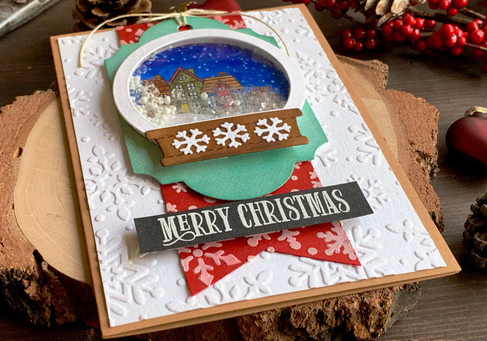 DIY Christmas card with a shaker snow globe filled with beads and background with stamped Christmas village at night. 