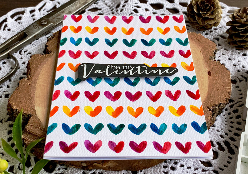 Handmade card for Valentine's day with a colourful background with hearts painted using watercolours. 