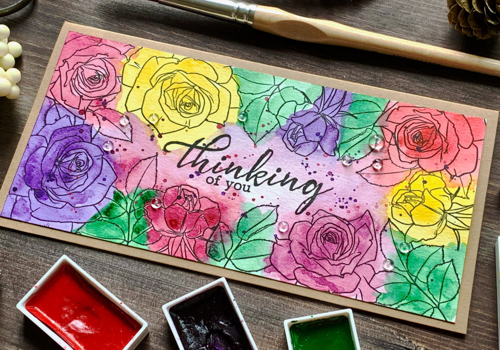 Handmade card with stamped roses along the edges creating frame and coloured with watercolours in multiple colours - pinks, purples, reds, yellows and greens - doing the messy watercolour technique.