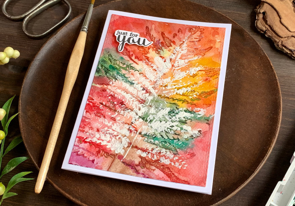Handmade autumnal greeting card with leaf pattern created by using real leaves and watercolours to create impressions and a white gouache to stamp a leaf over the pattern. One card has a typical autumnal background the other is purple, pink and blue.