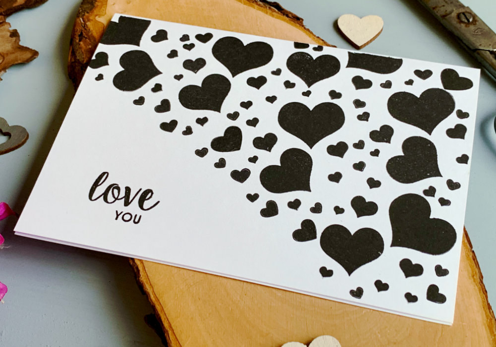 Simple handmade Valentine's day card with hearts stamped with a black ink on a white card base diagonally in the top half of the card and greeting that says Love You stamped in black in the lower section of the card.