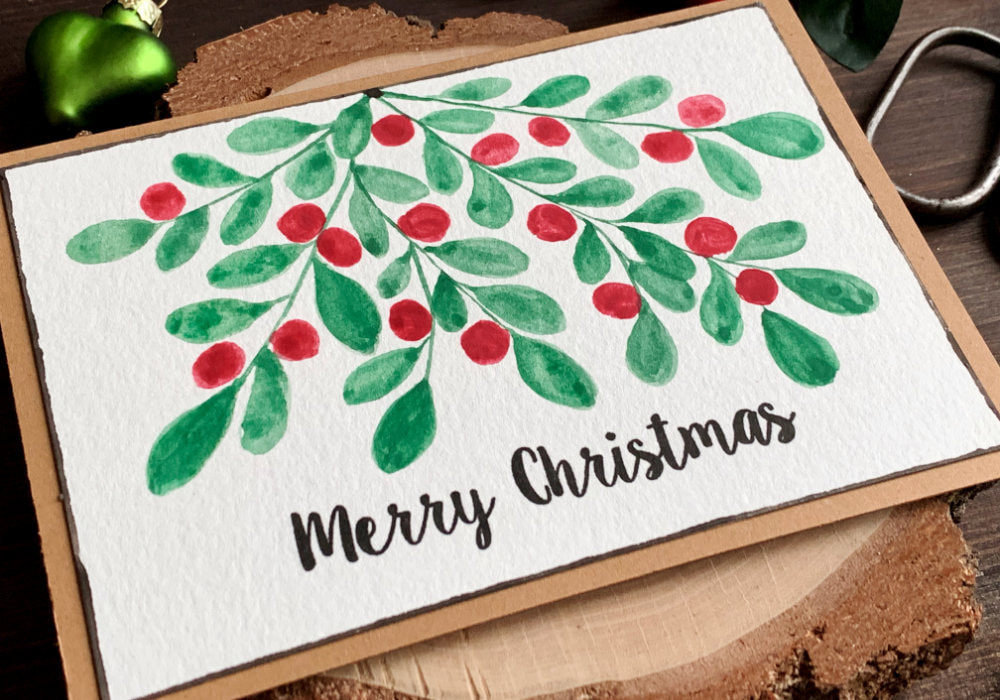 Simple Christmas card with a hand painted watercolour mistletoe with red berries and greeting that is stamped in black and says Merry Christmas.
