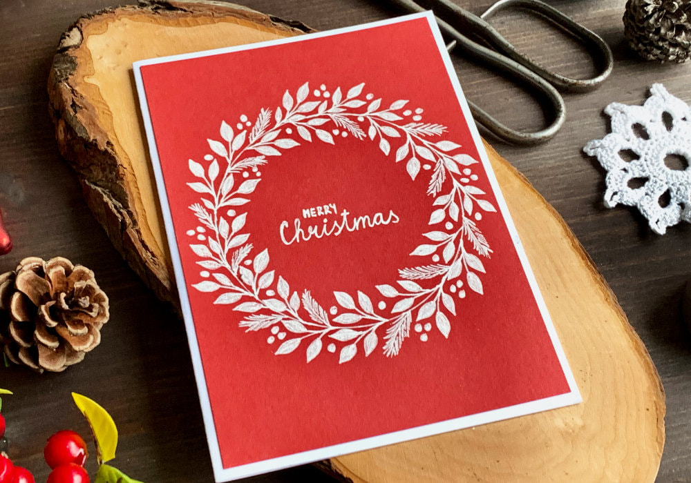 Simple DIY Christmas card with a hand-drawn wreath using a white gel pen and red card stock.