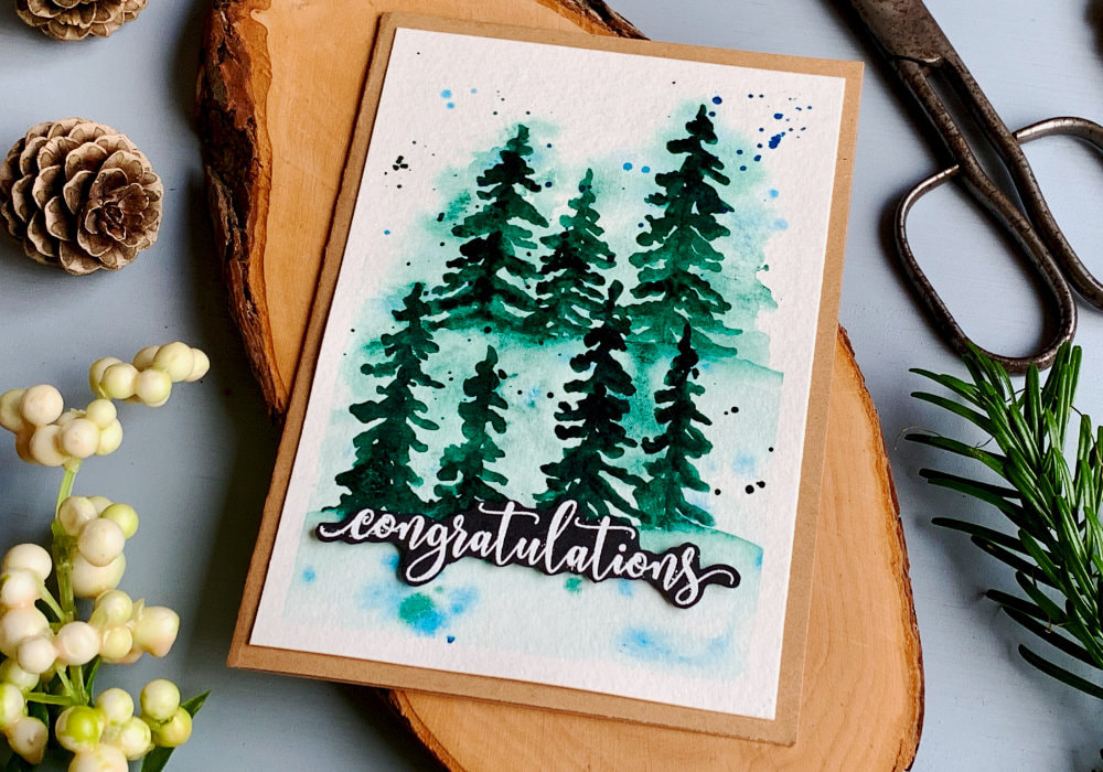 Handmade greeting card with a background with loose watercolour forest of green fir trees over a blurry watercolour background and a greeting that says Congratulations and is stamped and heat embossed in white on a black card stock, cut into a banner.