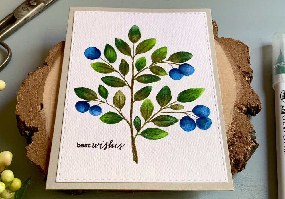 A handmade card with a blueberry branch that is hand drawn and painted using waterbased markers and a greeting stamped in black saying Best Wishes. 