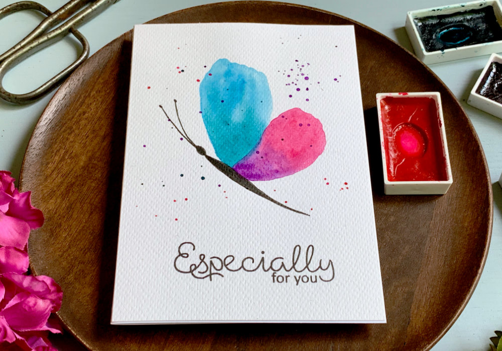 Handmade card for Birthday with a hand painted simple watercolour butterfly from a side with top wing in the blue-green and lower wing pink-purple. And black body. Painted on a white watercolour card stock, with a black greeting saying Especially For You.