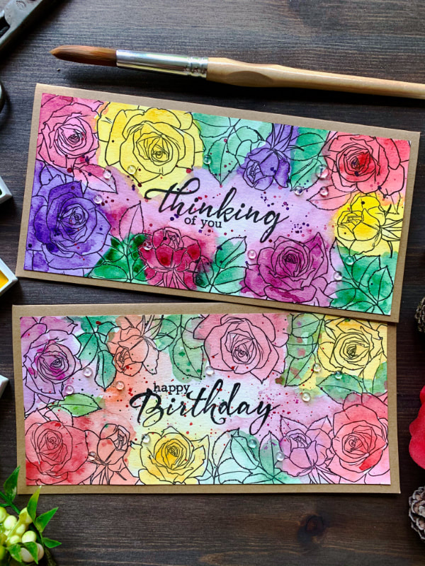 Handmade card with stamped roses along the edges creating frame and coloured with watercolours in multiple colours - pinks, purples, reds, yellows and greens - doing the messy watercolour technique.