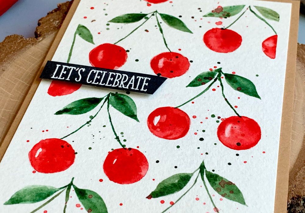 Handmade greeting card with a watercolour cherry background painted with watercolours and a greeting that says Let's Celebrate.