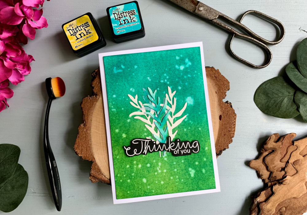 Handmade greeting card with a blue-green colour combination using the Tim Holtz Distress Mini Ink Pads Peacock Feathers and Mustard Seed. In the middle are three die-cut leaf branches and a greeting that says Thinking Of You.