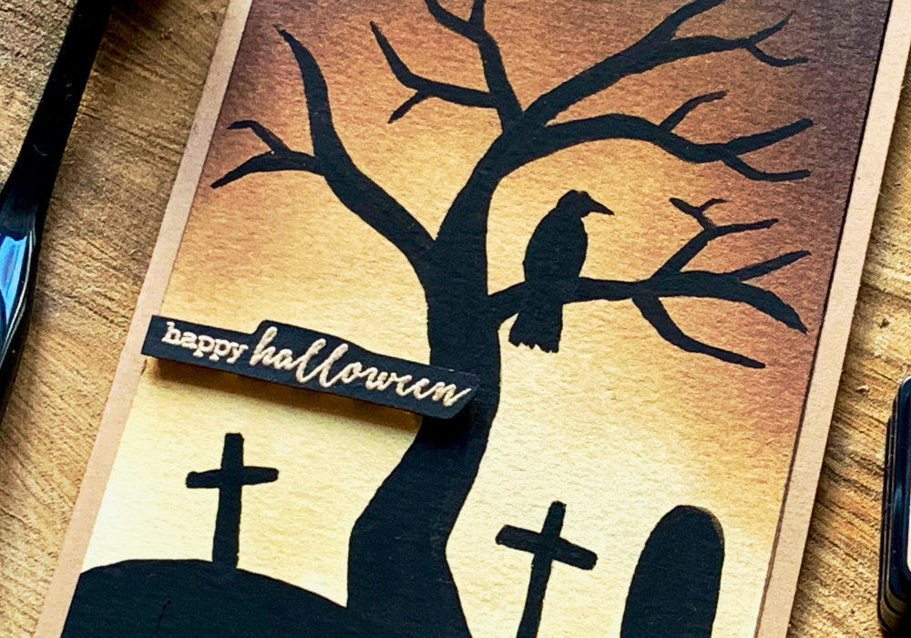 Halloween card with a brown Distress ink background and a black tree silhouette, a raven and a grave yard using gouache.