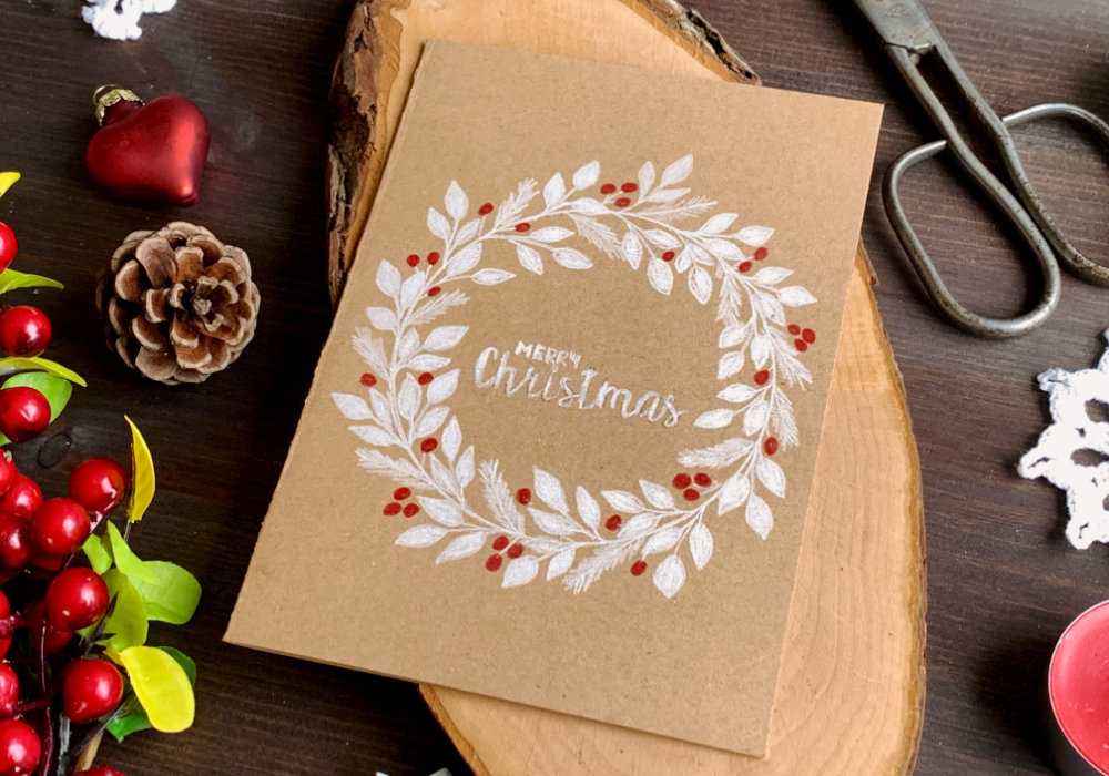 Simple DIY Christmas card with a hand-drawn wreath using a white pencil for the leaves, red pencil for berries and card base made out of a craft card stock.