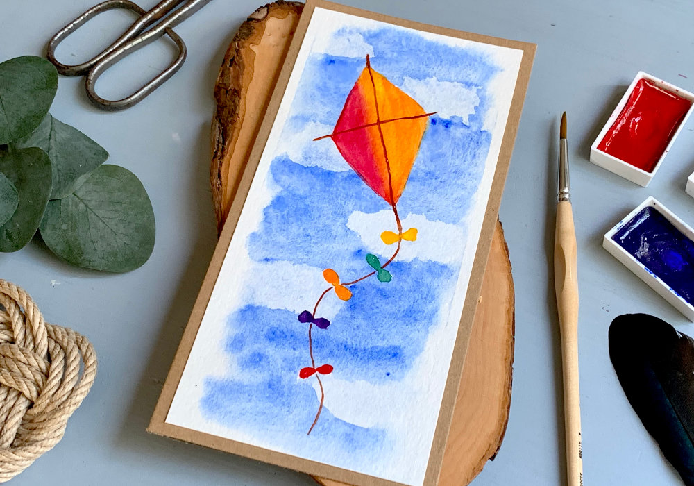 Handmade greeting card with a hand-drawn kite, painted with watercolours flying in the sky. 