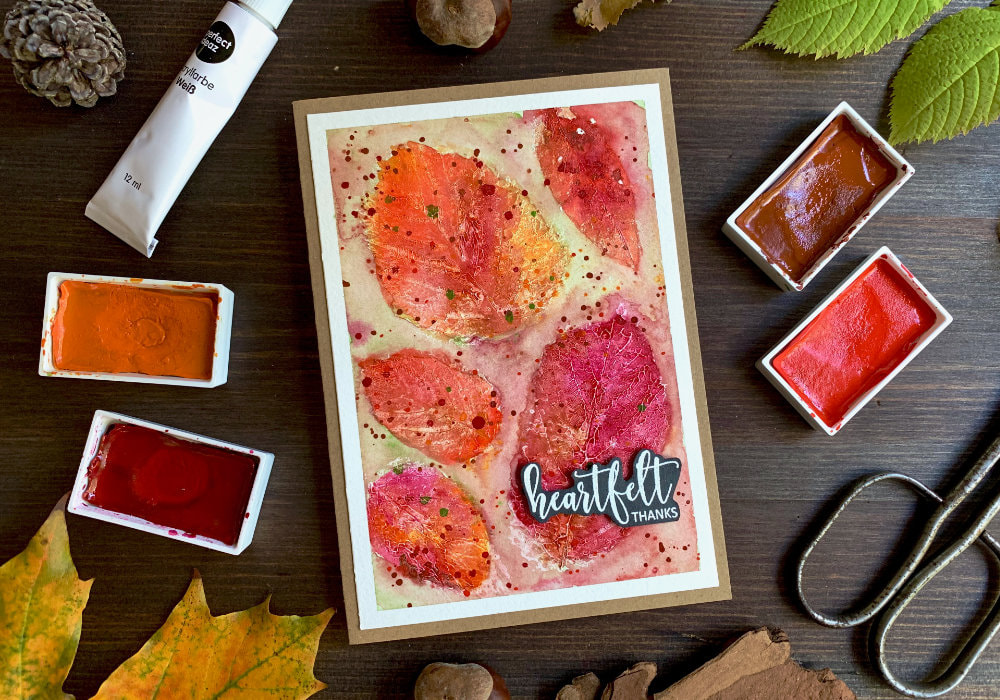 Handmade card with a background stamped with leaves using white acrylic paints and coloured with watercolours in orange, brown, red and magenta to create autumnal Thank You card. 