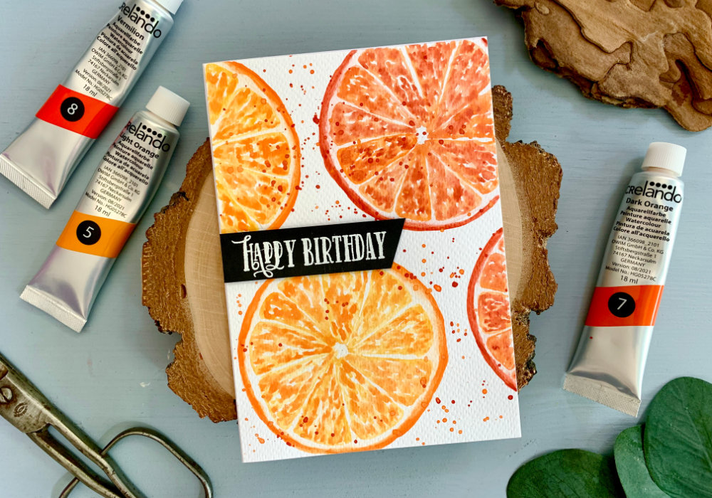 Handmade Birthday card with a background of citrus orange slices painted using watercolours and a greeting saying Let's celebrate.