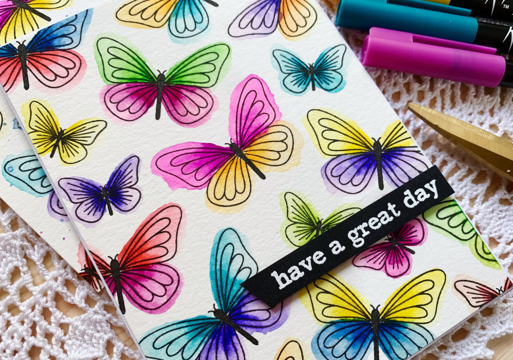A colourful butterfly card featuring a simple stamped background using individual stamps and messy watercolour technique using water based brush markers.