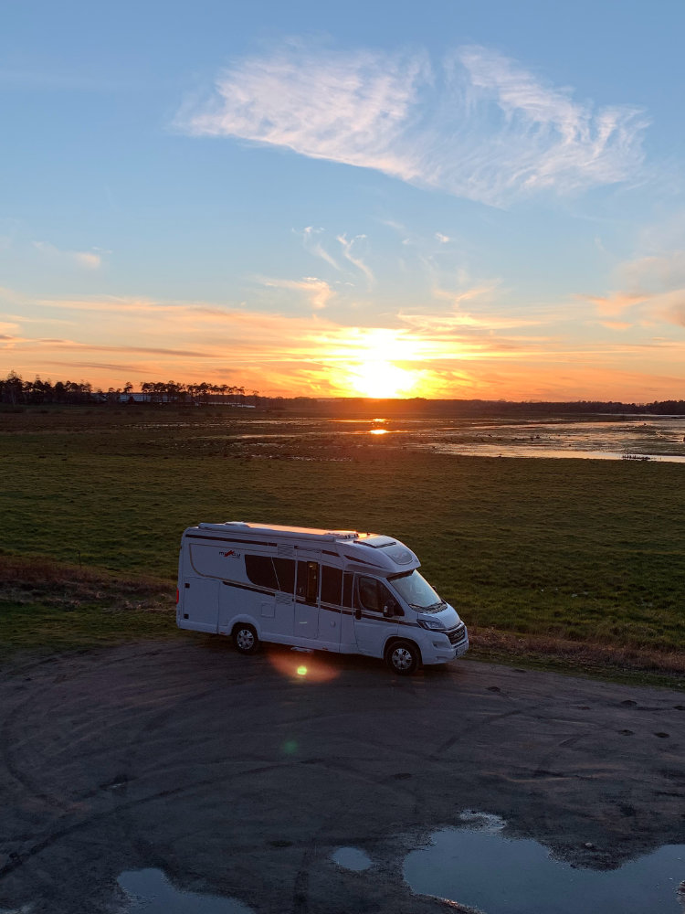 Our van parked at a picnic area next to a feeld during sundown, with the sun setting in the background.