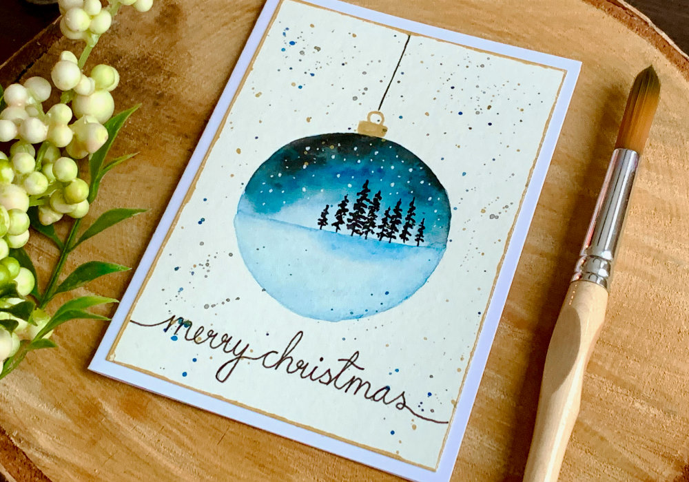 Handmade Christmas card with an ornament decoration with watercolour landscape.