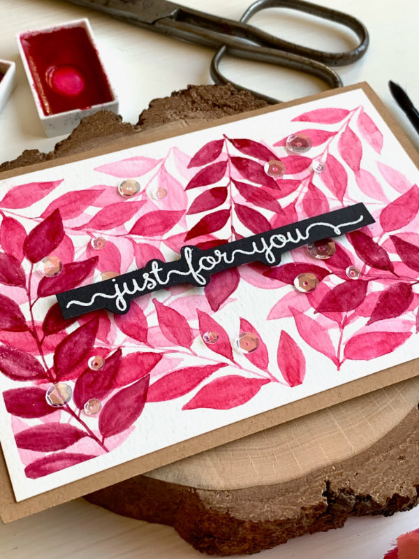 Handmade card with a leaf background painted with watercolours, layered on top of each other using three shades of pink and a greeting banner saying 